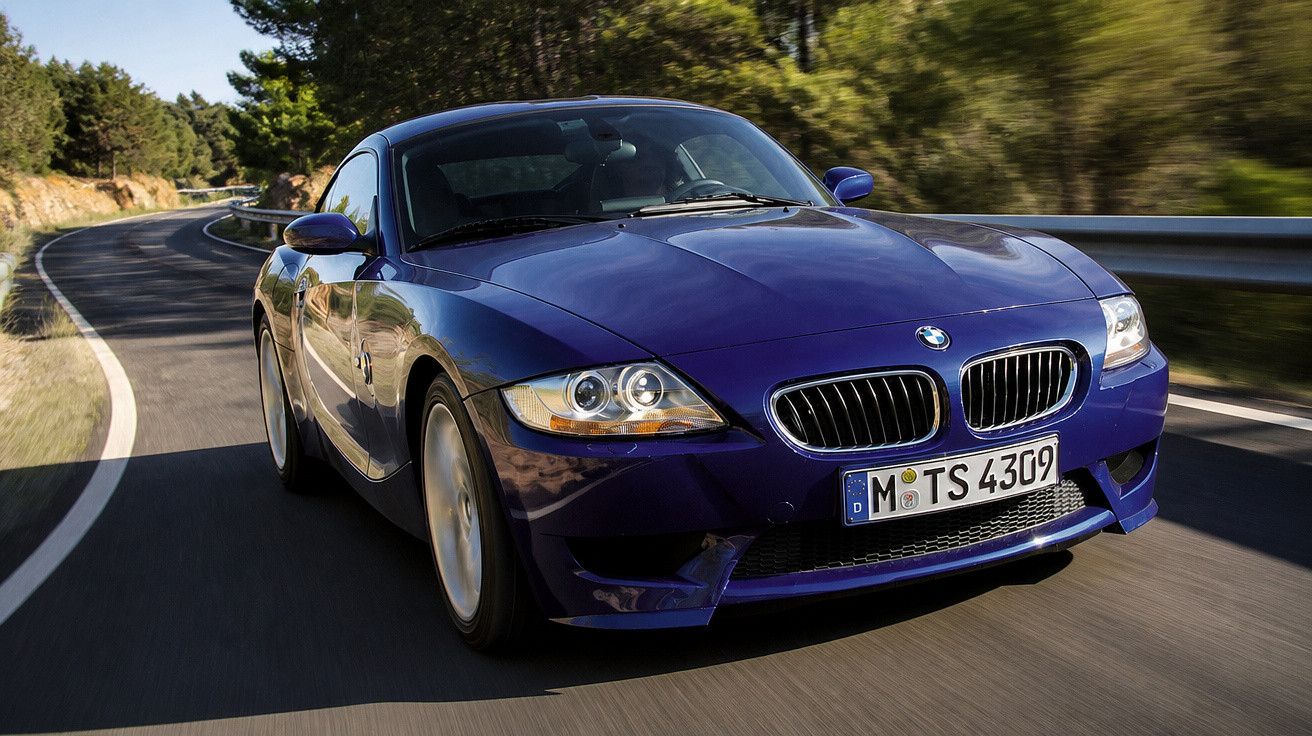 Carro desportivo azul BMW a circular numa estrada sinuosa rodeada de árvores e vegetação.