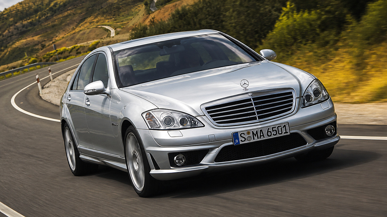 Carro Mercedes-Benz Prateado em estrada curva com paisagem montanhosa ao fundo.