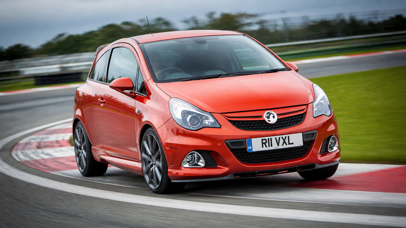 Carro desportivo vermelho em curva numa pista de corrida sob um céu nublado.