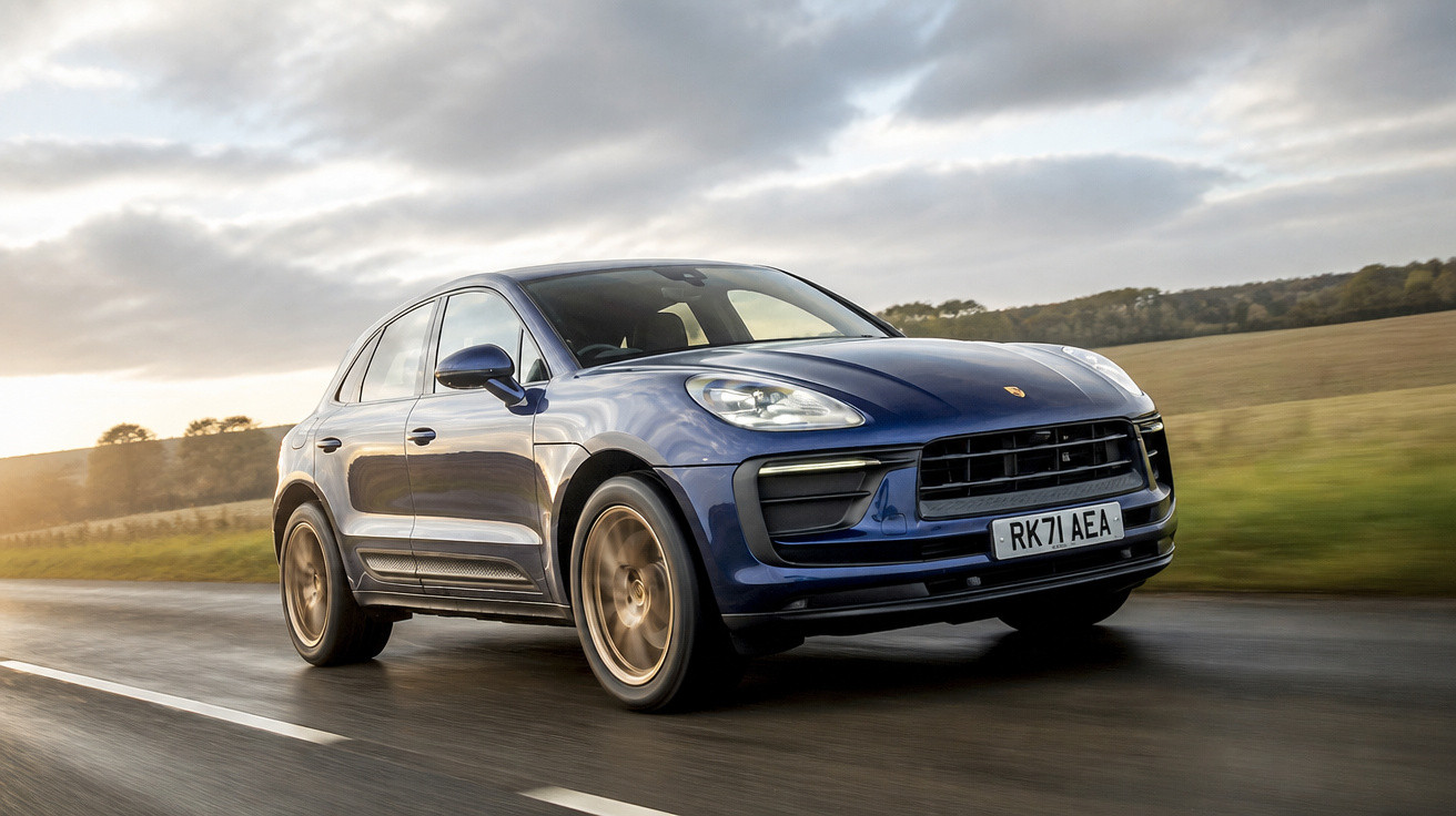 Carro SUV azul Porsche a circular numa estrada rural sob céu nublado ao pôr do sol.