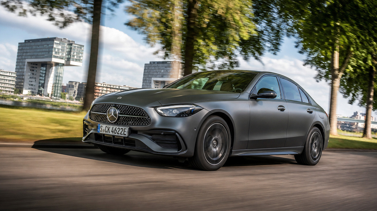 Automóvel Mercedes-Benz cinza a circular numa estrada urbana com árvores e edifícios modernos ao fundo.