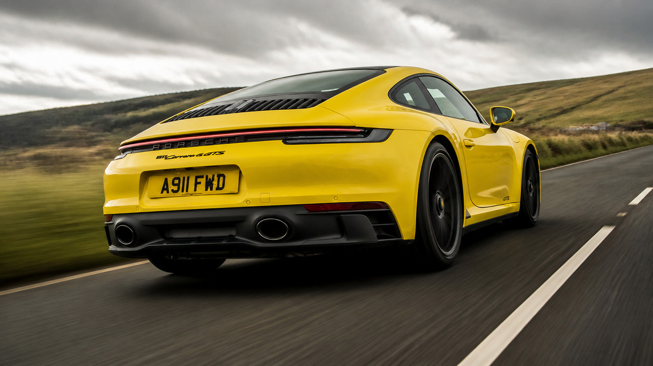 Carro desportivo amarelo Porsche 911 em estrada rural sob céu nublado.