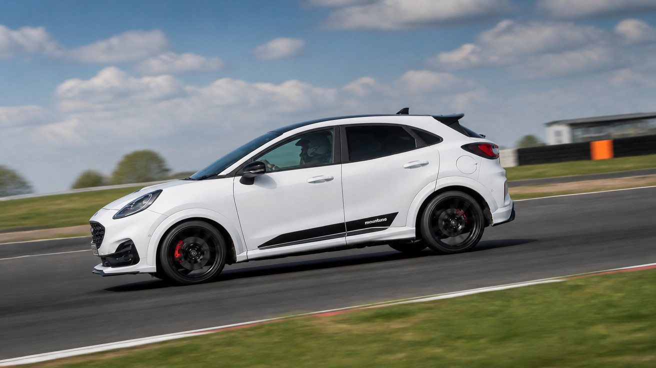 Carro sport branco a alta velocidade numa pista de corrida sob céu azul com nuvens.