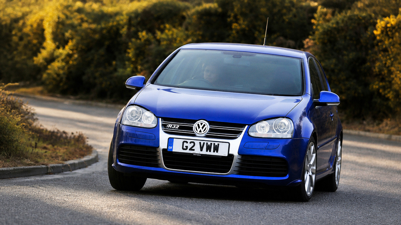 Carro azul Volkswagen R32 a conduzir numa estrada curva rodeada de vegetação amarela.